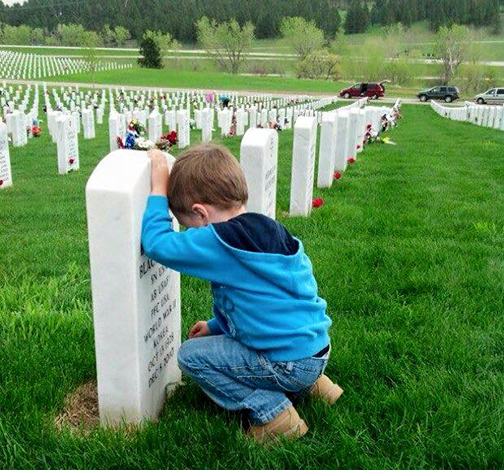 [Photo of a small boy kneeling in a military cemetery]