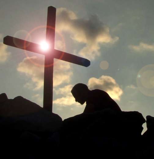 Photo of a man kneeling at the foot of a cross