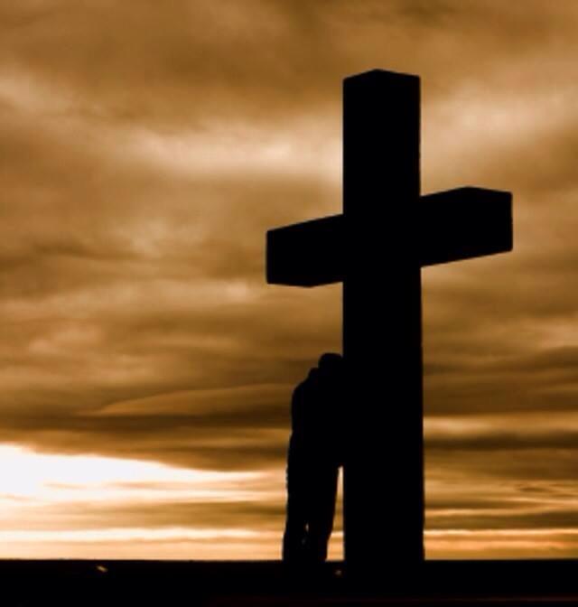 [Photo of a man leaning against a large cross]